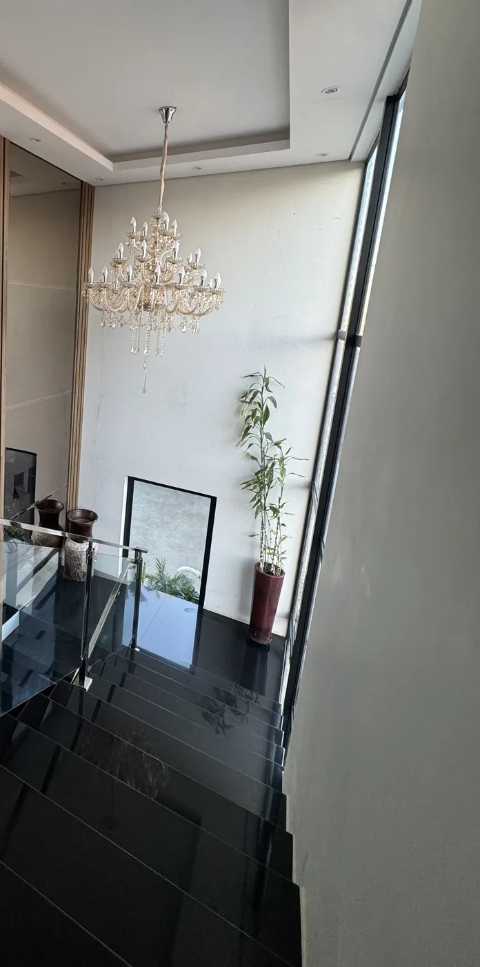 Escada de degraus pretos com guarda-corpo de vidro e lustre de cristal no pé-direito duplo
