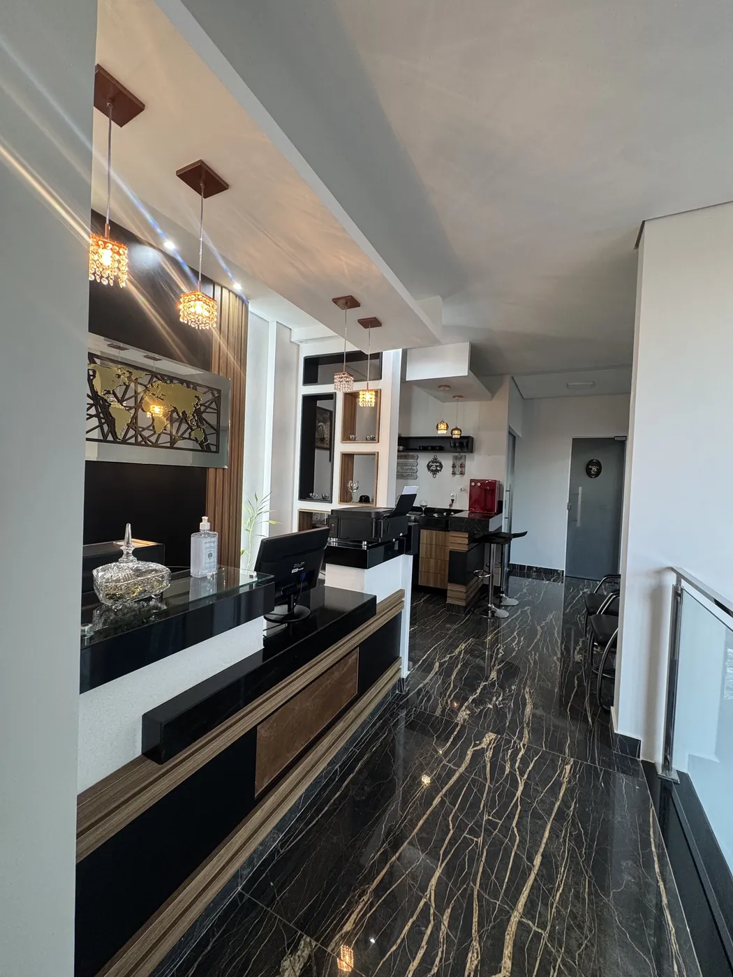 Recepção com balcão preto e madeira, pendentes de cristal e piso de mármore negro com veios dourados