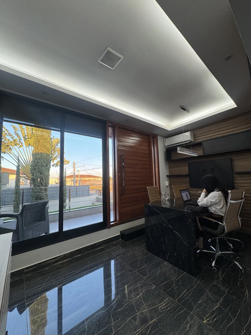Sala com mesa de mármore negro, porta de madeira, forro com luz de sanca e porta de vidro para a varanda