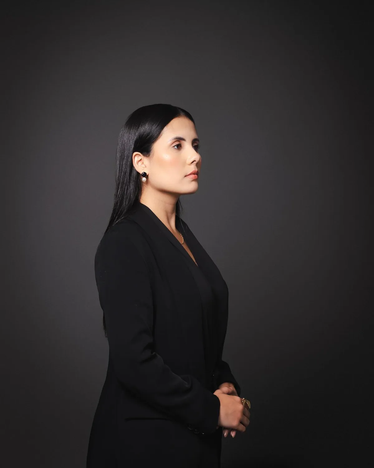 Andressa Xavier, advogada, de perfil, de blazer preto, em fundo escuro